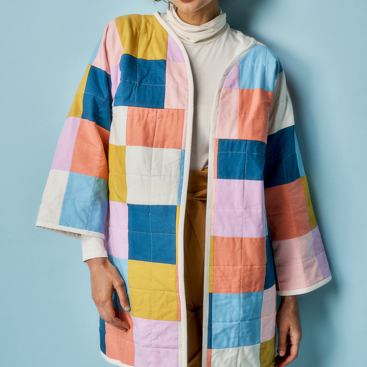 Person wearing a colorful checkered coat against a light blue background