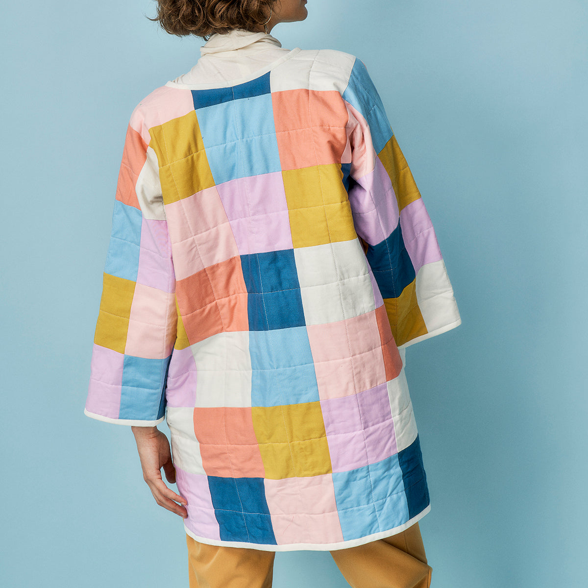 Person wearing a colorful quilted jacket against a light blue background