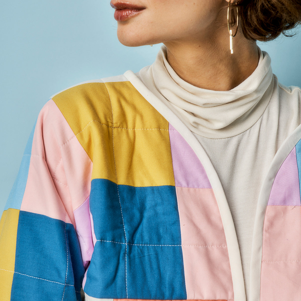 Person wearing a colorful patchwork jacket with a blue background