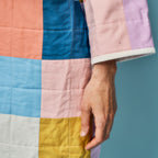 Multicolored quilt with a hand holding it against a blue background