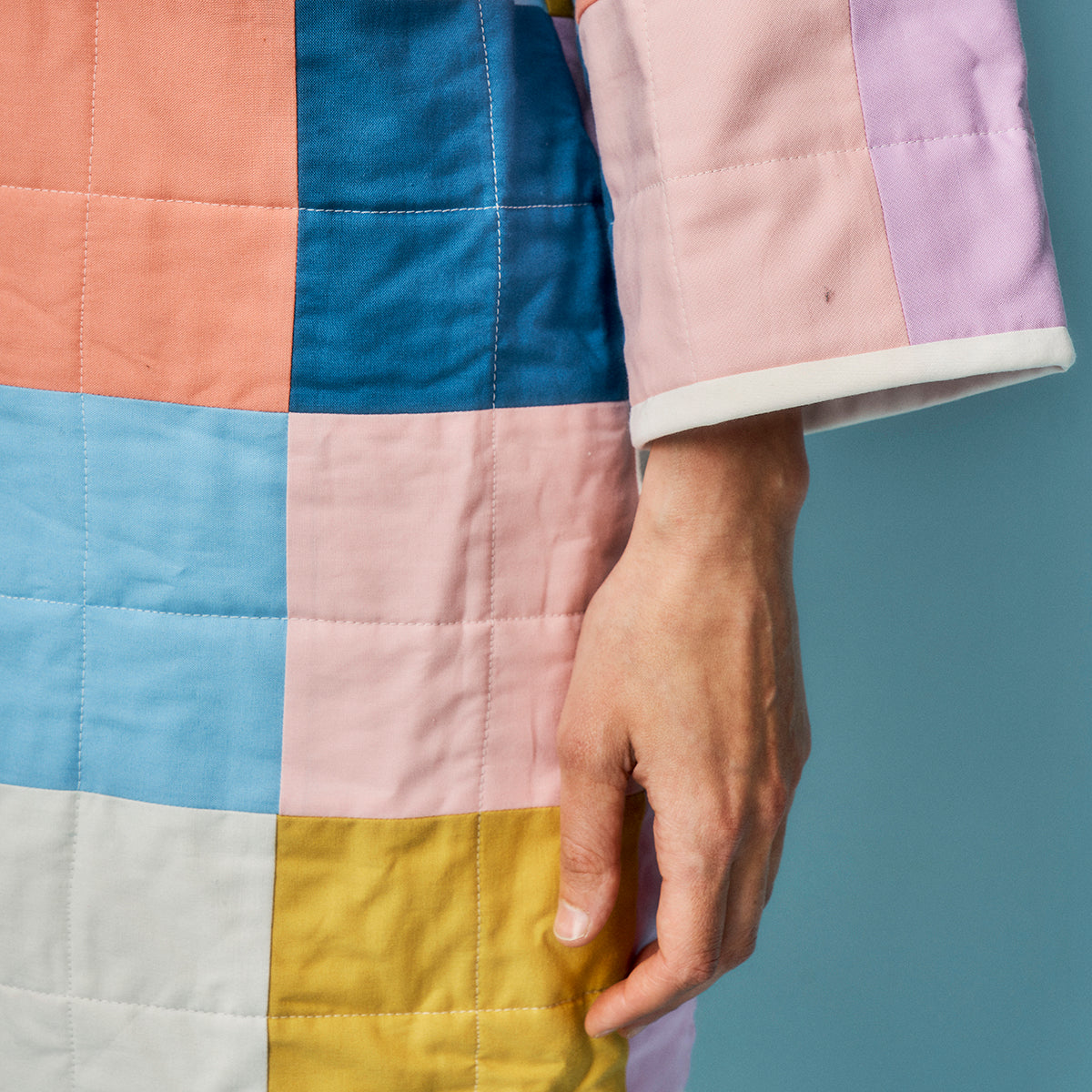 Multicolored quilt with a hand holding it against a blue background