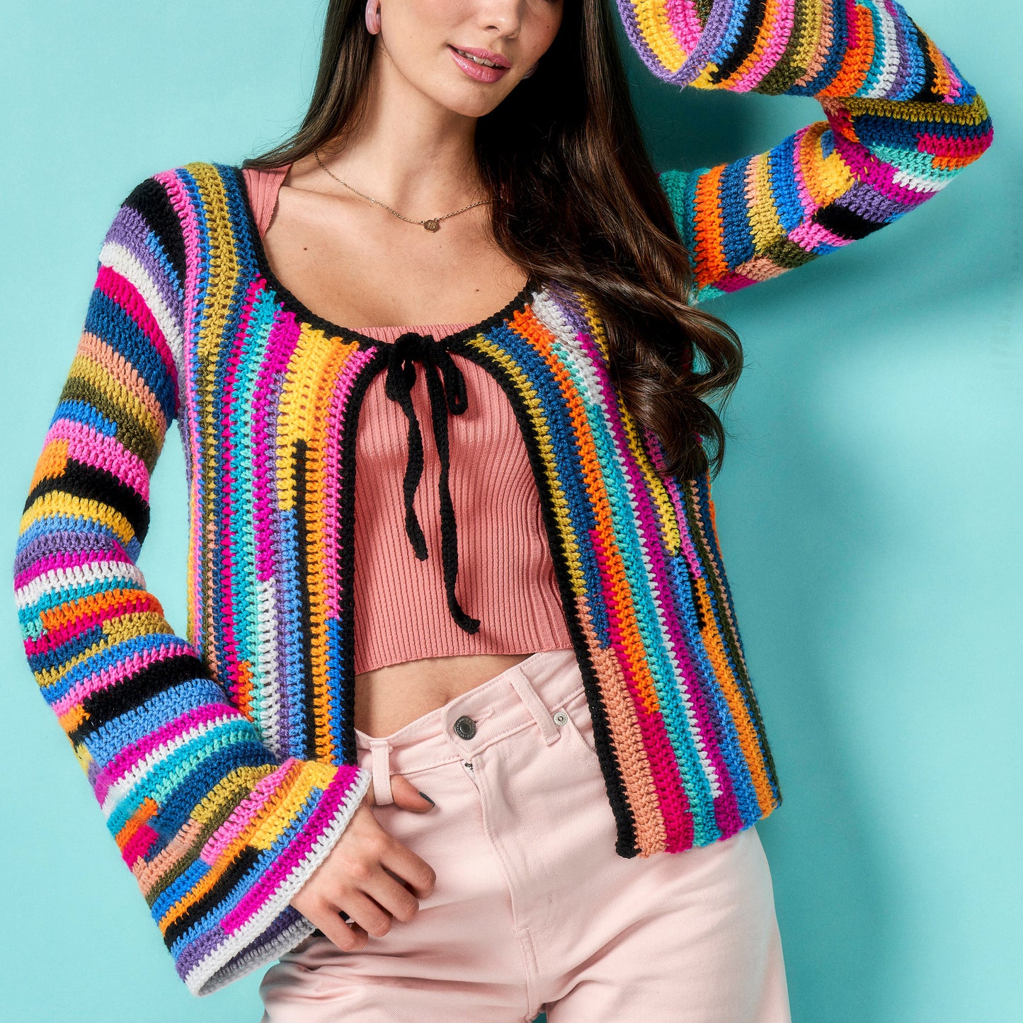 Woman wearing a colorful striped crochet cardigan against a blue background