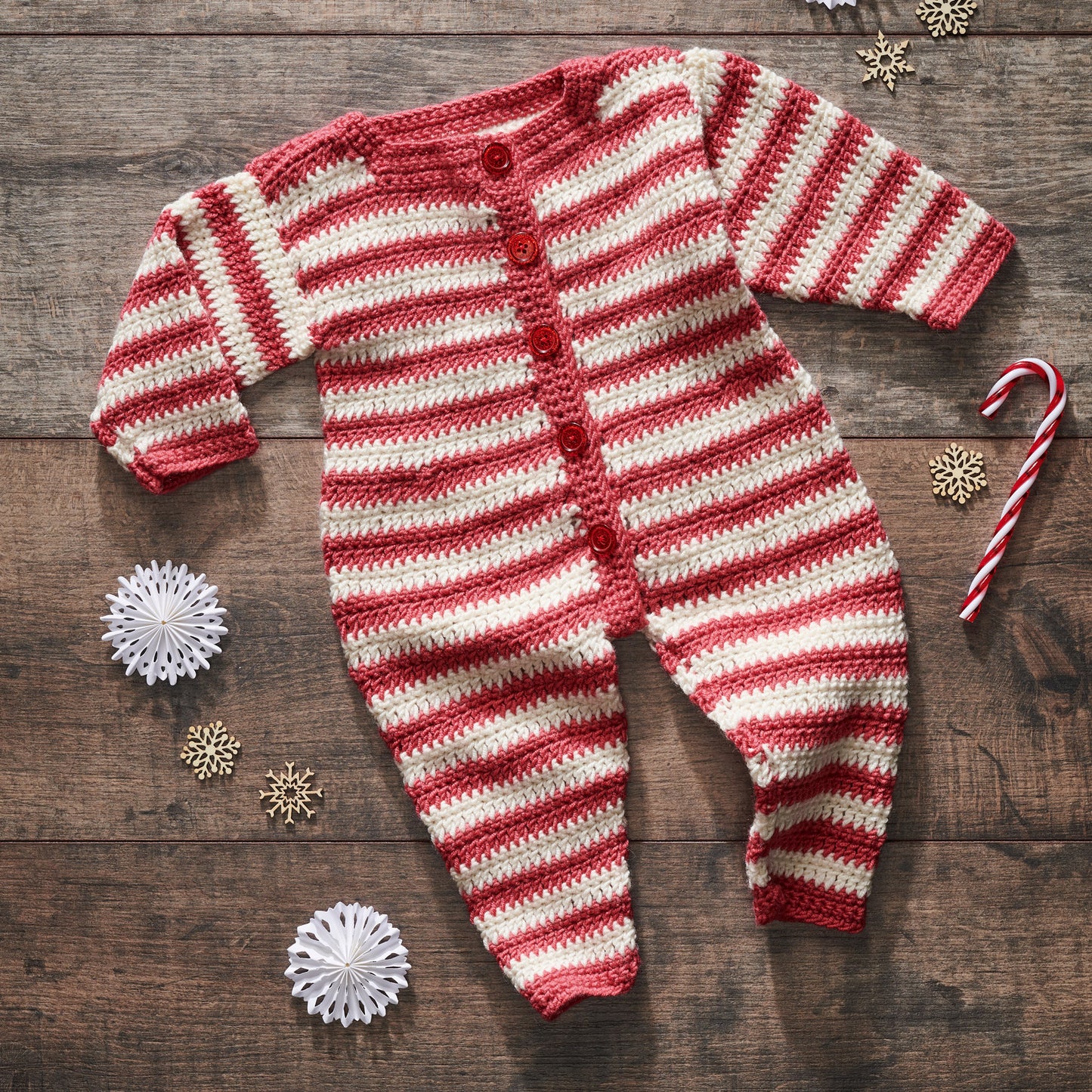 Red and white striped baby onesie on a wooden surface with Christmas decorations.