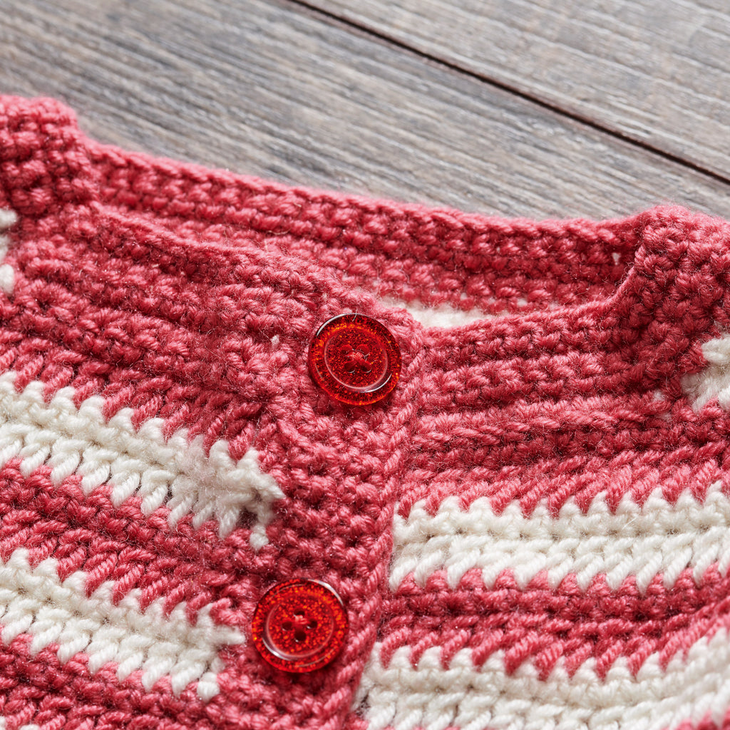 Close-up of a pink and white crochet garment with red buttons on a wooden surface