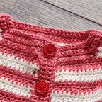 Close-up of a pink and white crochet garment with red buttons on a wooden surface