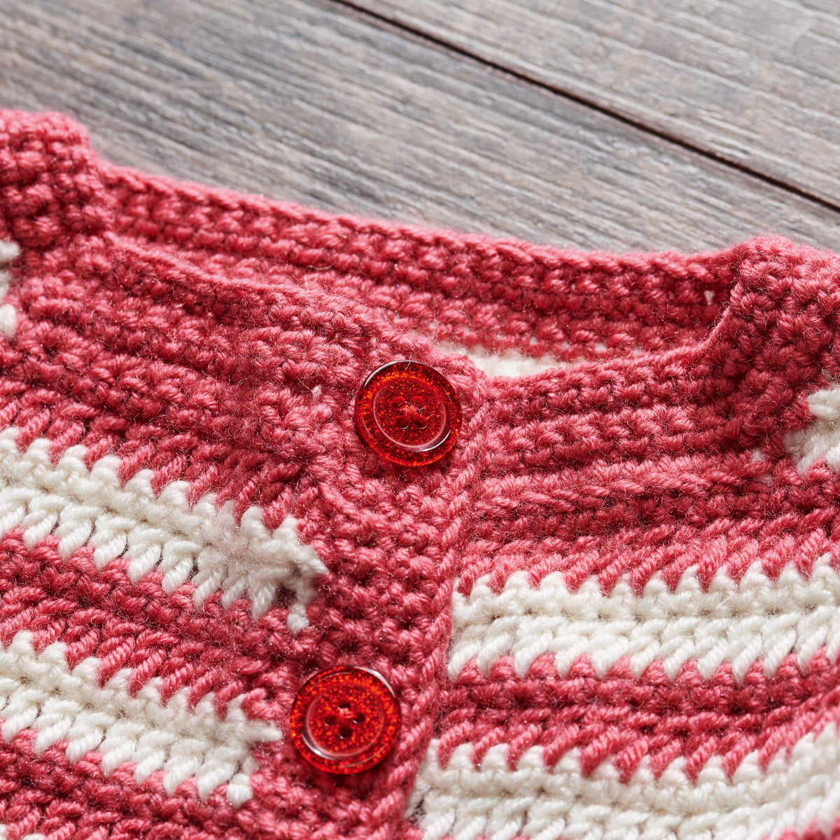 Close-up of a pink and white crochet garment with red buttons on a wooden surface
