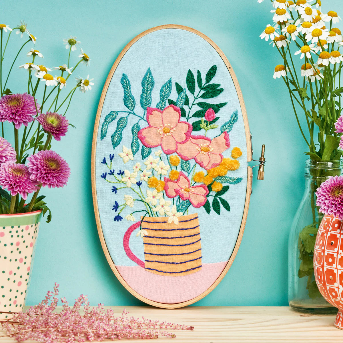 Embroidery hoop with floral design on a teal background with flowers around