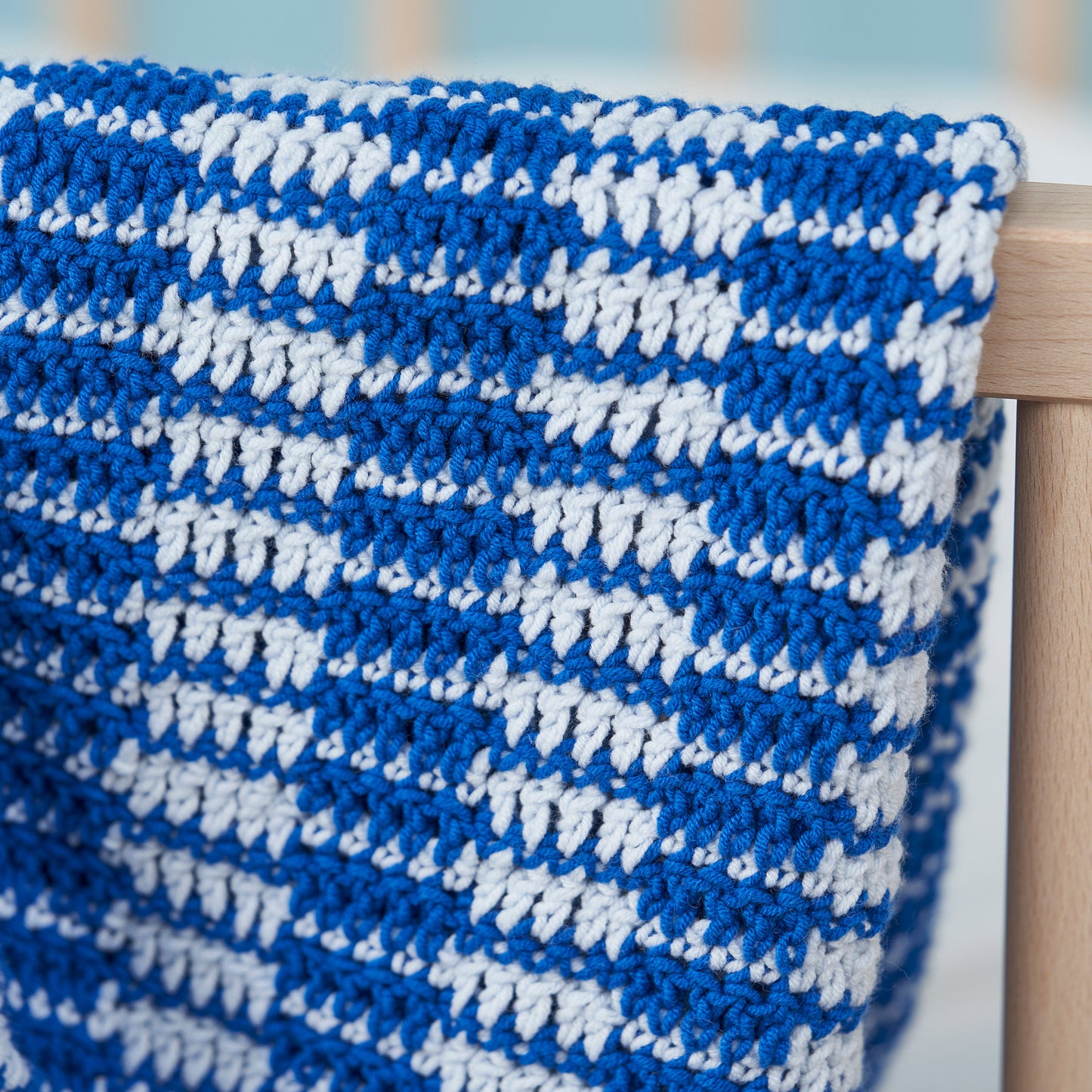 Blue and white crocheted blanket on a wooden chair with a blurred background