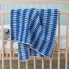 Blue and white checkered blanket draped over a crib with a teddy bear.