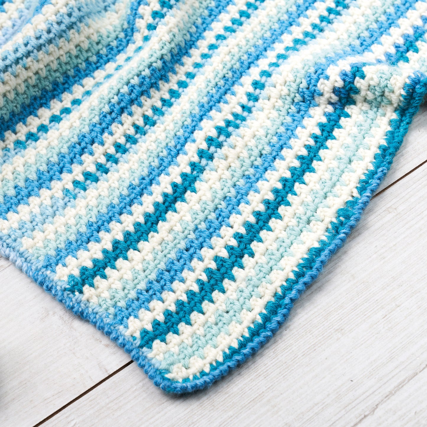 Blue and white striped crochet blanket on a wooden surface