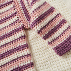Close-up of a crocheted blanket with pink and purple stripes on a white background