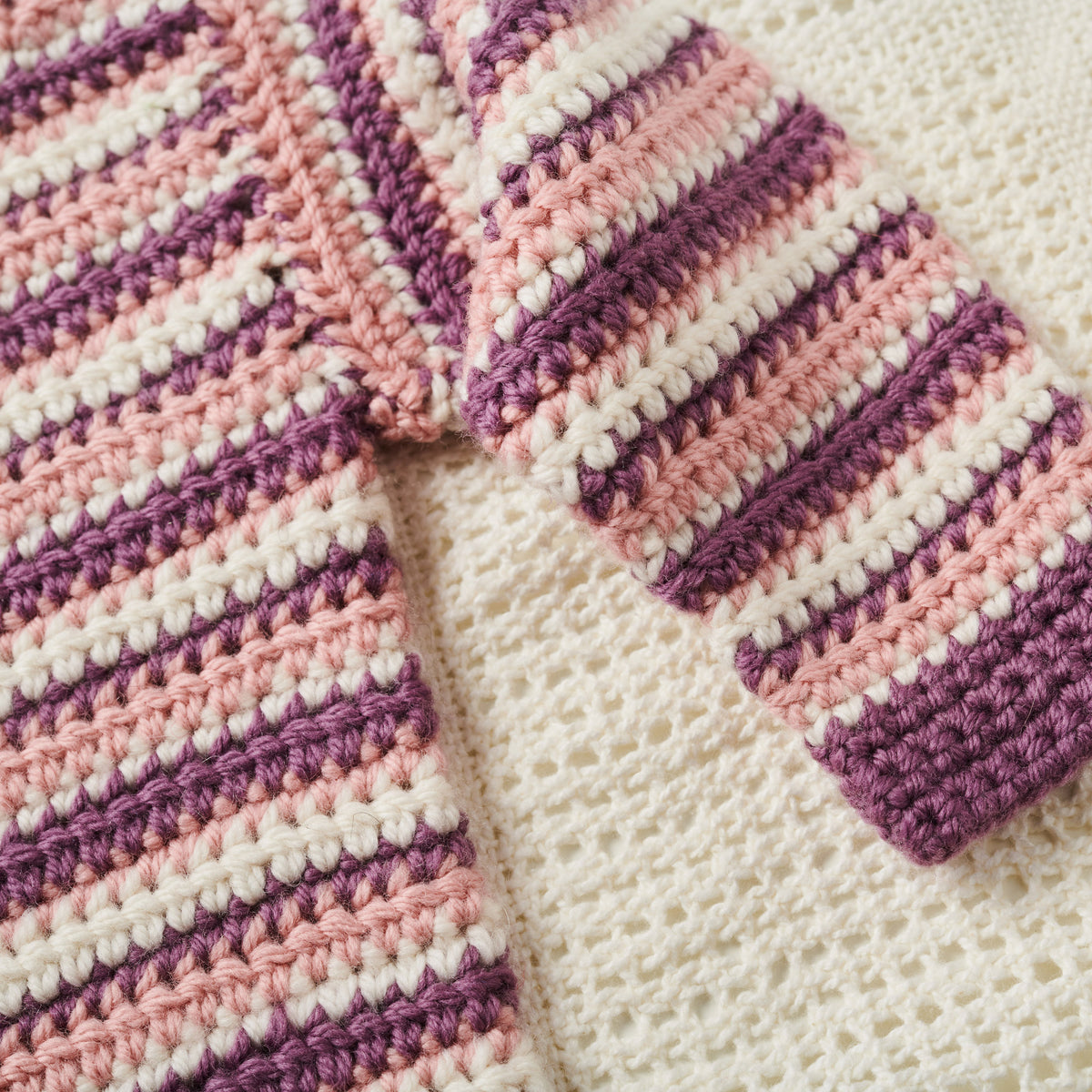Close-up of a crocheted blanket with pink and purple stripes on a white background