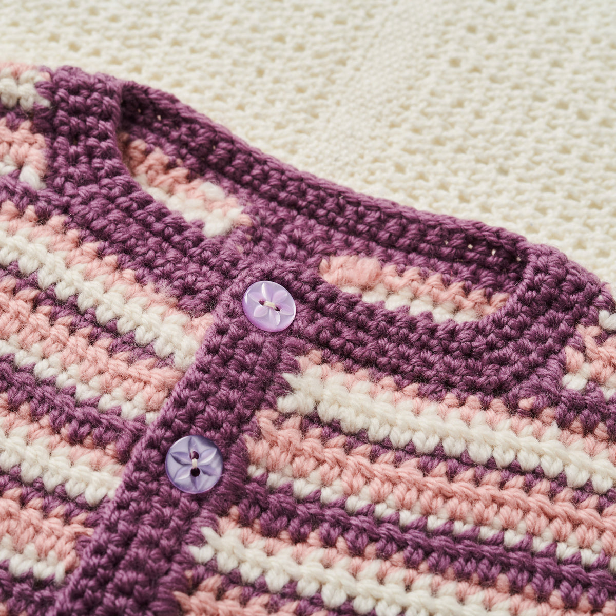 Close-up of a crocheted baby cardigan with buttons on a light background