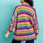 Person wearing a colorful striped crochet cardigan with floral patterns on a teal background