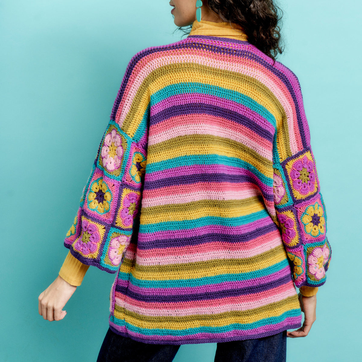 Person wearing a colorful striped crochet cardigan with floral patterns on a teal background