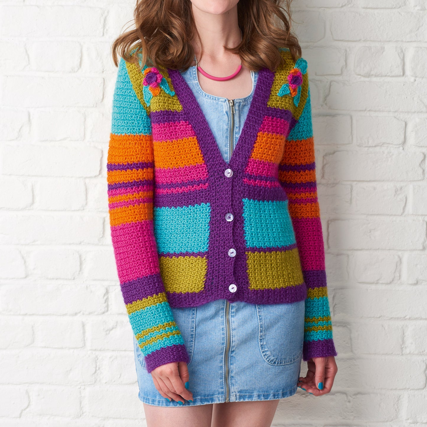 Person wearing a colorful striped cardigan against a white brick wall.