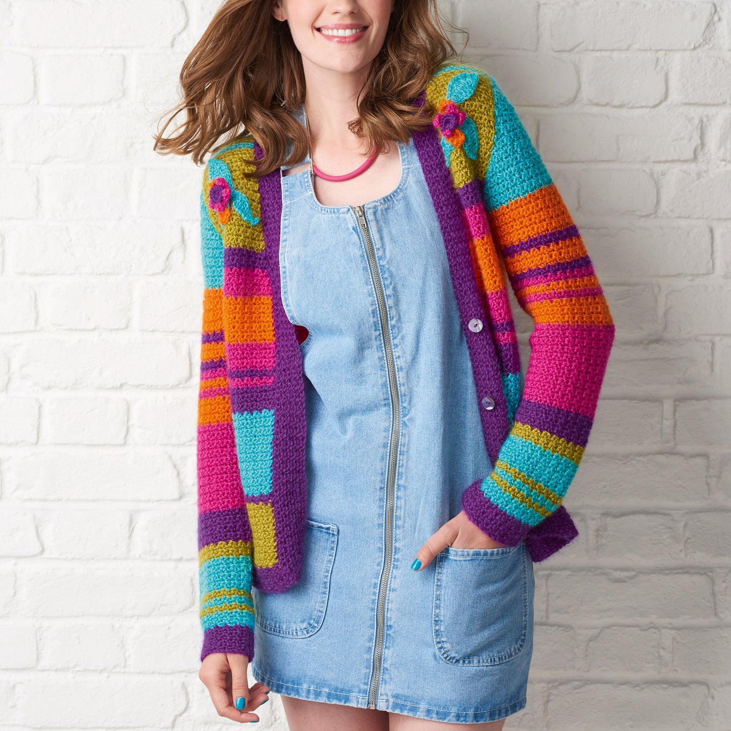 Woman wearing a colorful striped cardigan against a white brick wall.