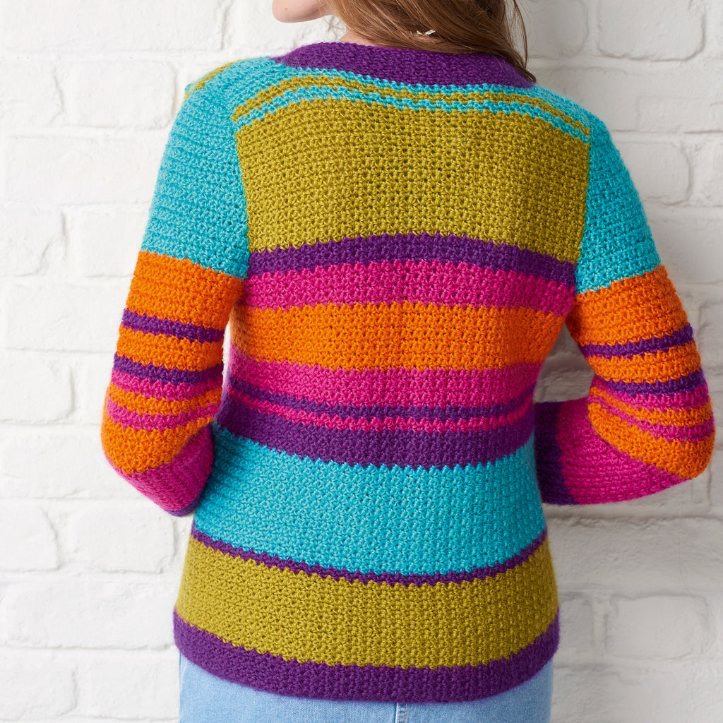 Colorful striped sweater worn by a person against a white brick wall.