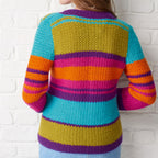 Colorful striped sweater worn by a person against a white brick wall.