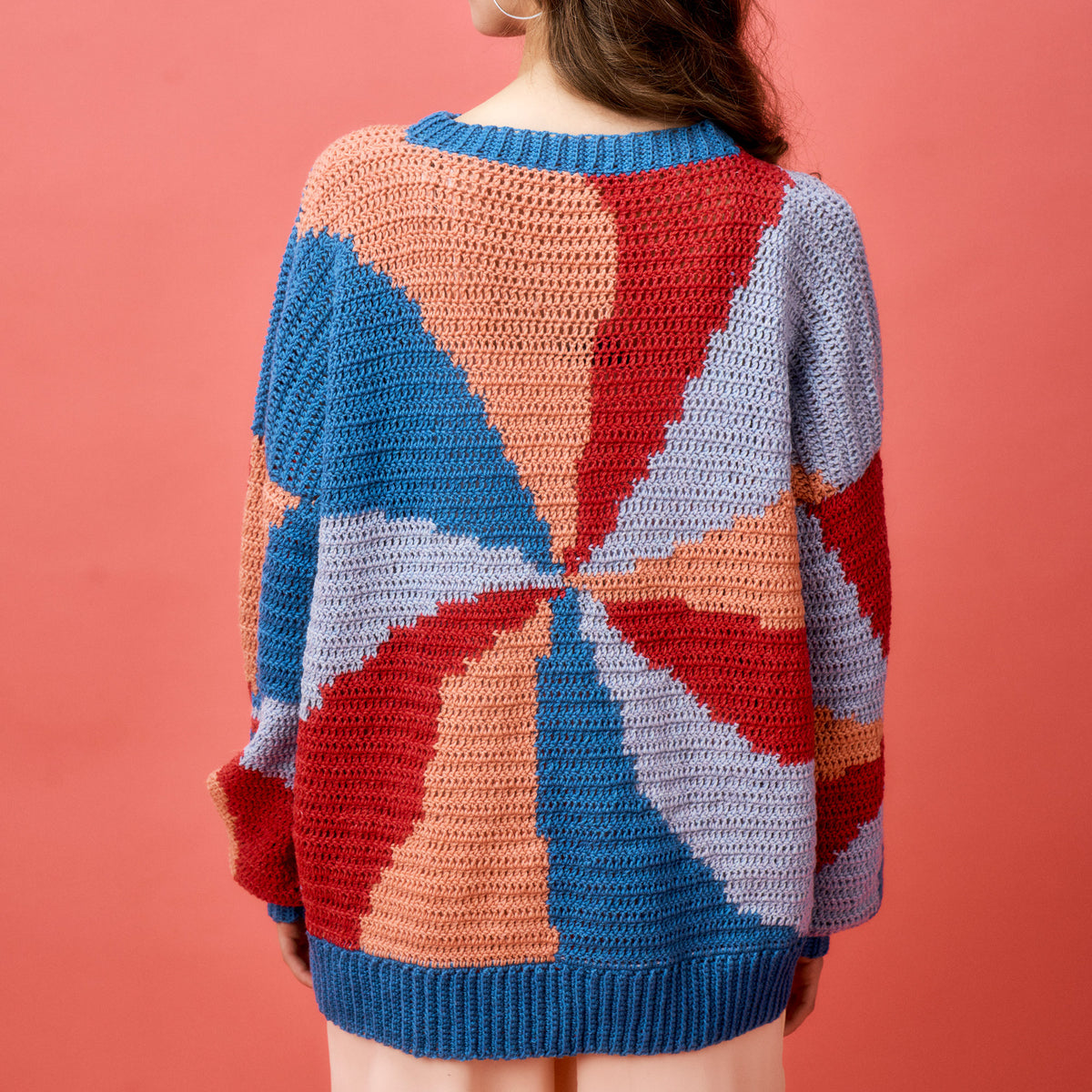 Person wearing a colorful geometric-patterned sweater against a pink background