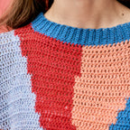 Close-up of a colorful crochet garment with blue, red, and pink patterns.