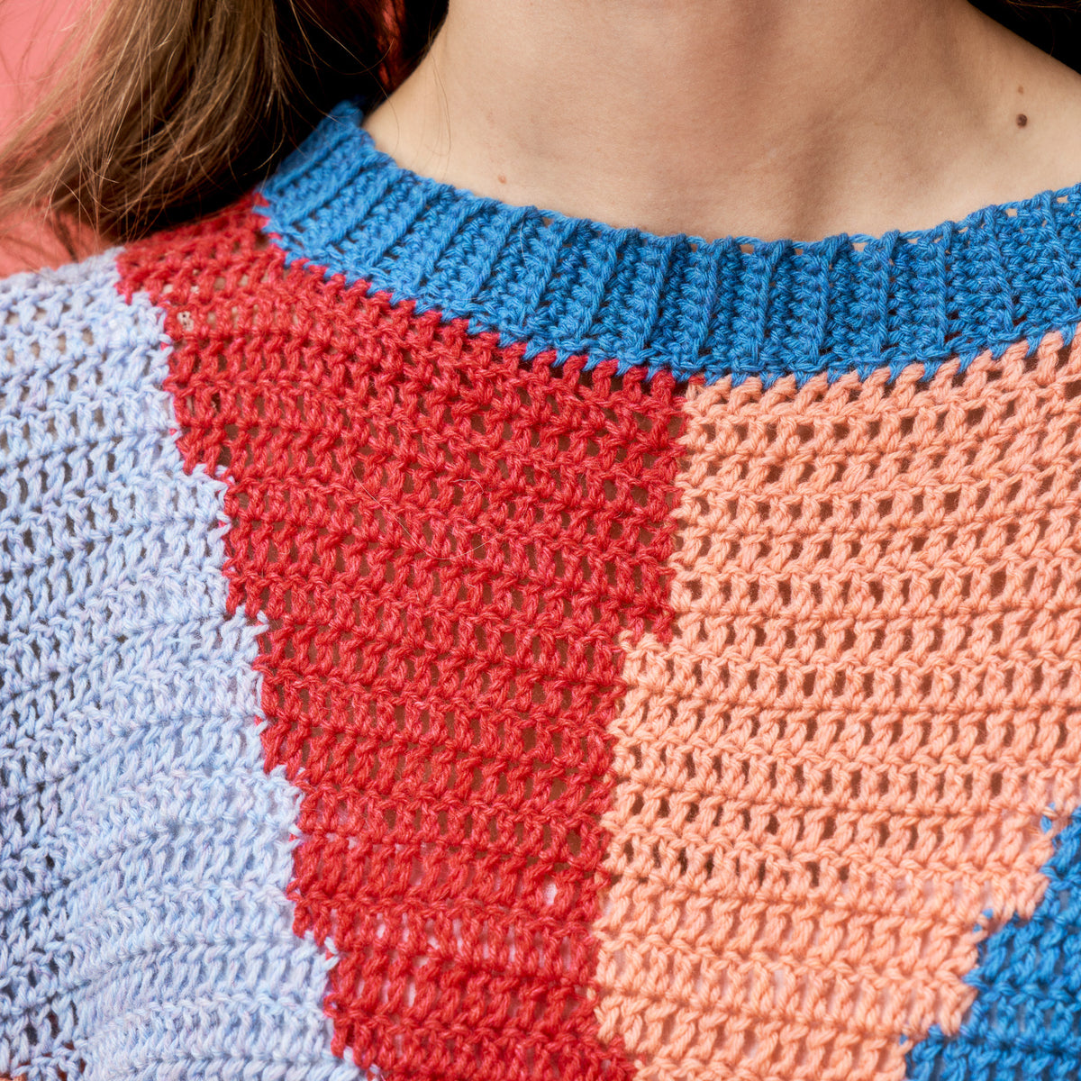 Close-up of a colorful crochet garment with blue, red, and pink patterns.