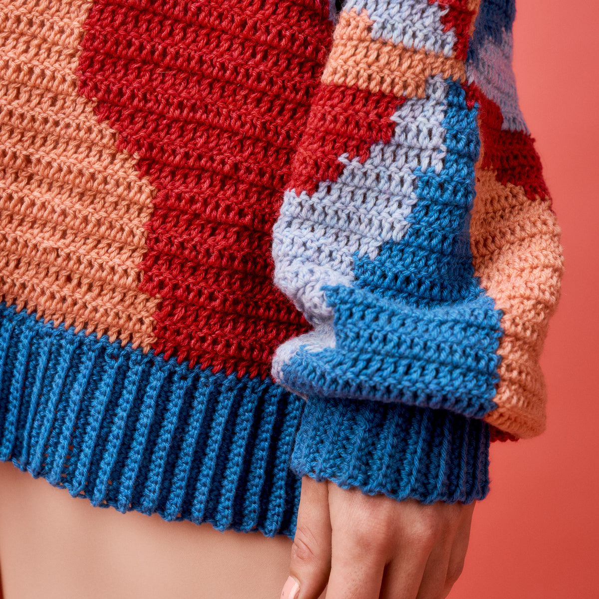 Close-up of a colorful knitted sweater with blue cuffs on a pink background
