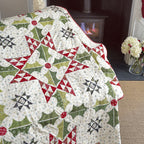 Quilt with geometric pattern draped over a chair in a room with a fireplace and flowers.