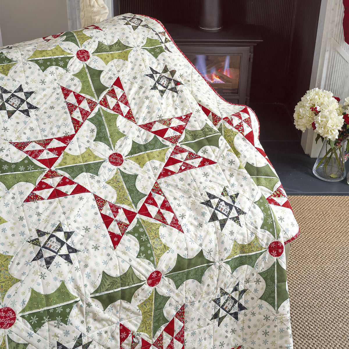 Quilt with geometric pattern draped over a chair in a room with a fireplace and flowers.