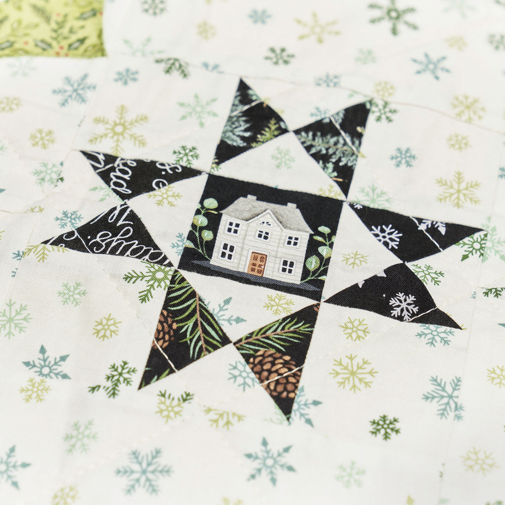Quilt block with house design and snowflakes on a white background