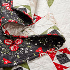 Quilt with floral and geometric patterns in red, black, and white on a white background