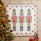 Decorative quilt with nutcracker design next to a Christmas tree