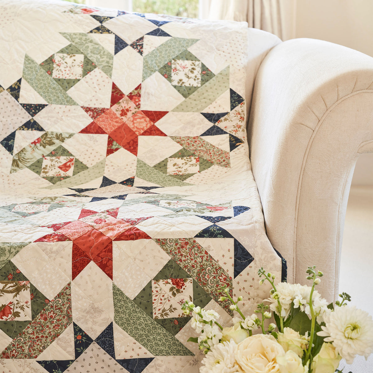 Quilt with geometric pattern draped over a sofa, accompanied by a vase of flowers.