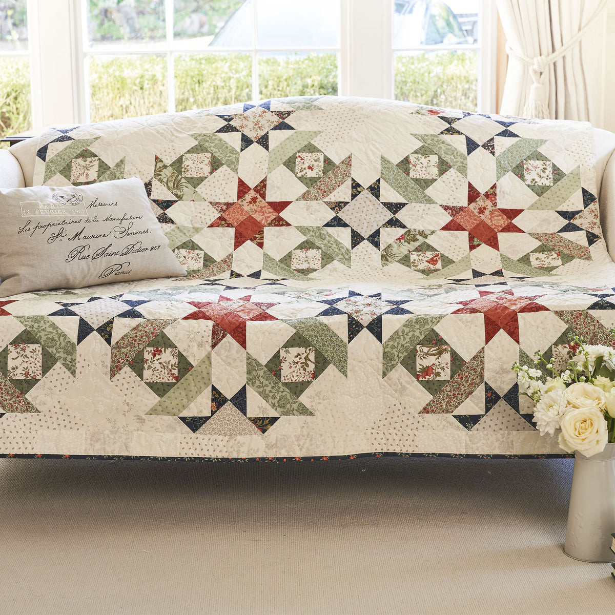 Quilted cover on a sofa with a floral arrangement in a room with large windows.
