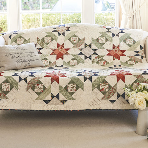 Quilted cover on a sofa with a floral arrangement in a room with large windows.