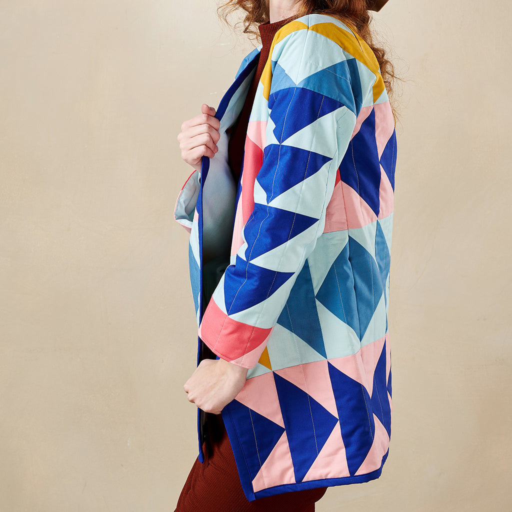 Person wearing a colorful geometric-patterned coat against a beige background