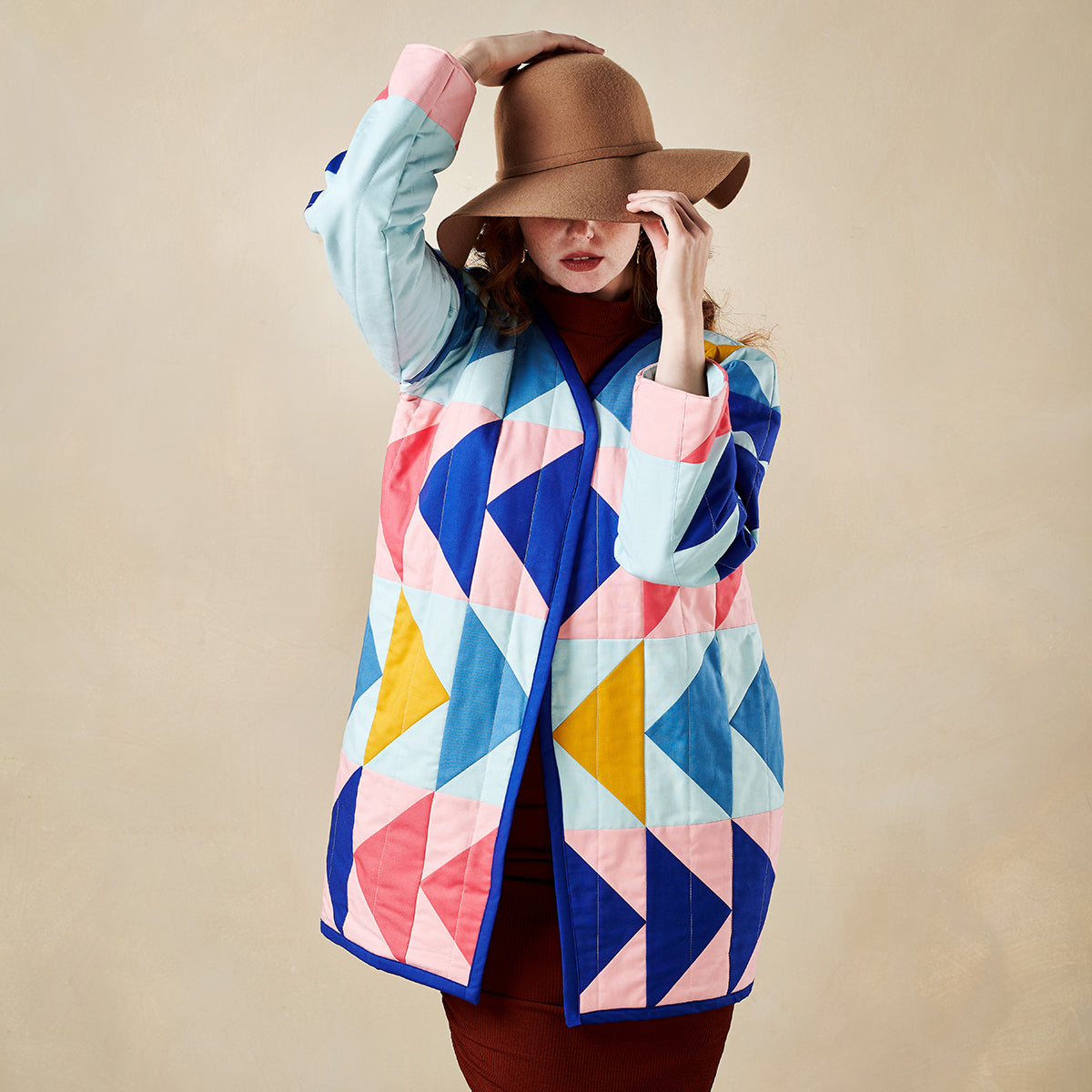 Woman wearing a colorful geometric-patterned coat against a beige background