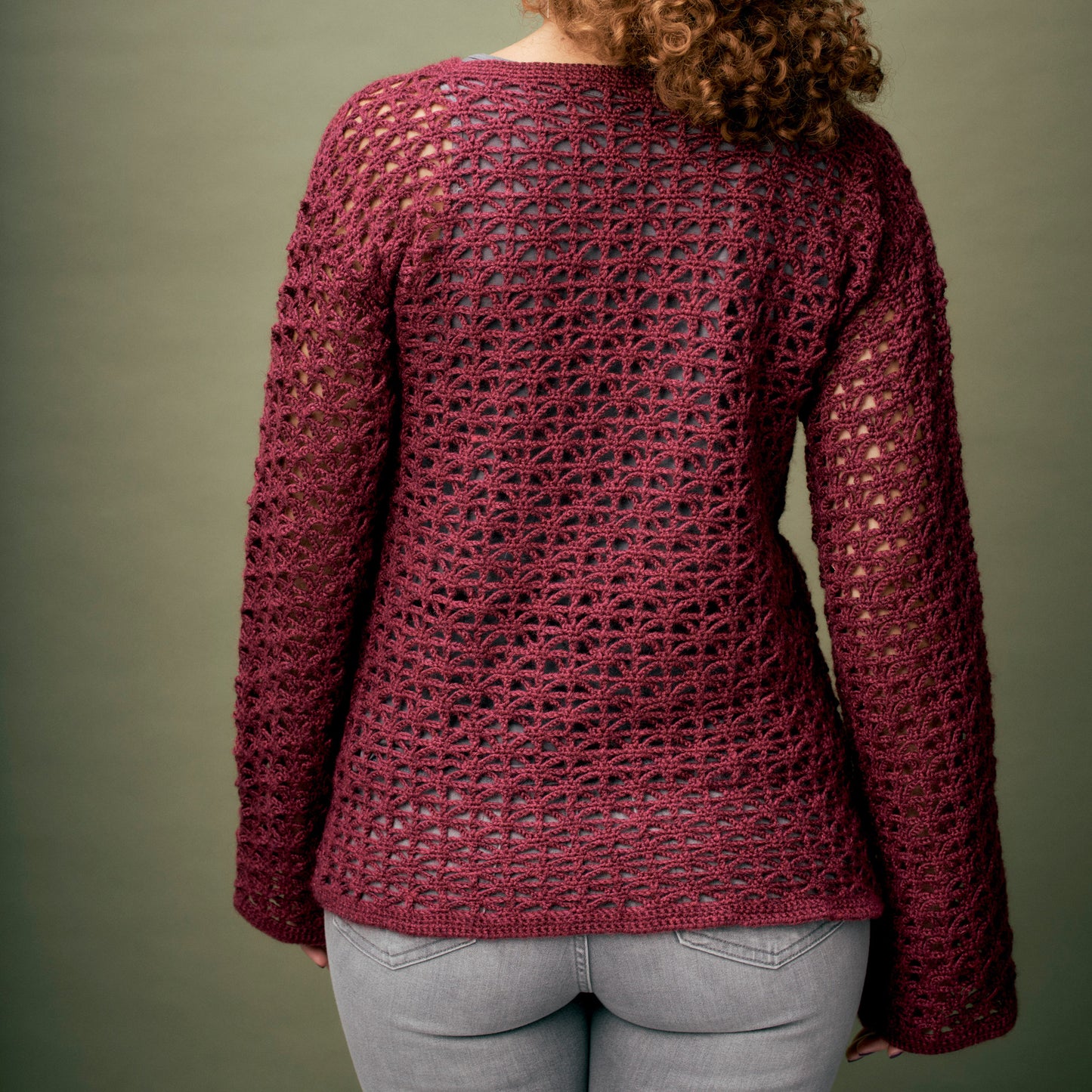 Person wearing a maroon crochet sweater against a green background