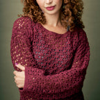 Woman wearing a maroon crochet sweater against a plain background