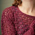 Close-up of a person wearing a maroon crocheted top with a neutral background
