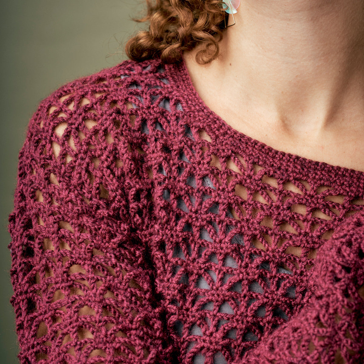 Close-up of a person wearing a maroon crocheted top with a neutral background