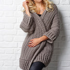 Person wearing a chunky knit gray sweater against a white brick wall.
