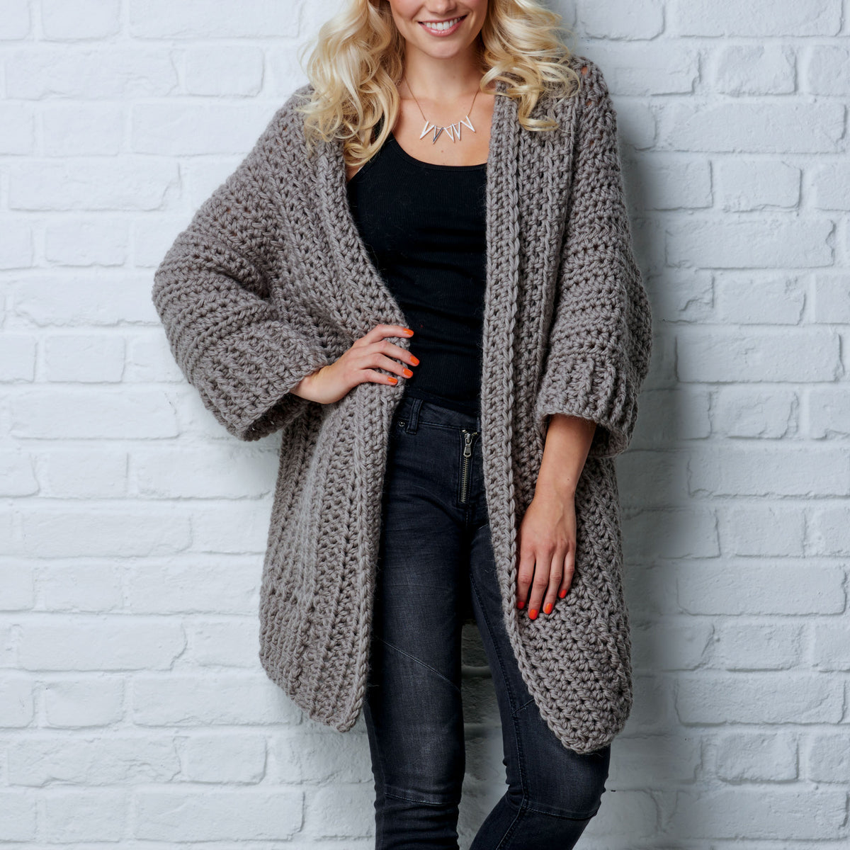 Woman wearing a chunky knit cardigan against a white brick wall