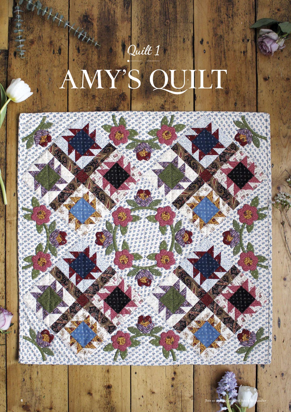 Floral patterned quilt titled "Amy's Quilt" on rustic wooden floor. Features geometric shapes and flowers in red, blue, and green. Elegant, cozy feel.