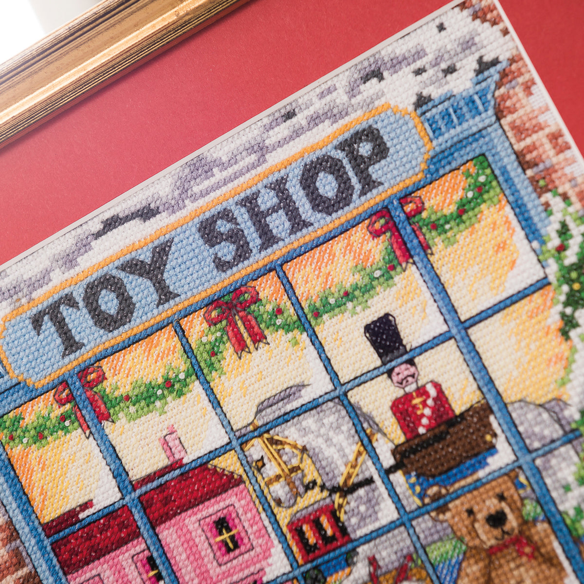 Cross-stitched panel of a toy shop with various toys and a red frame.