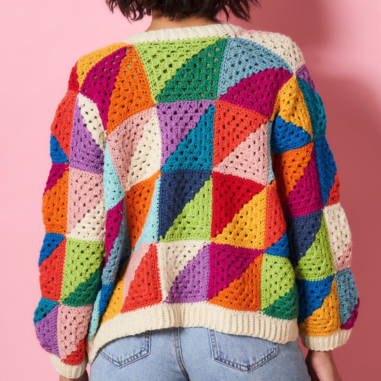 Colorful crocheted sweater with geometric pattern on a pink background