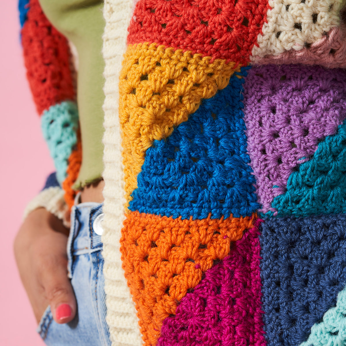 Colorful crocheted blanket with a patchwork pattern on a pink background