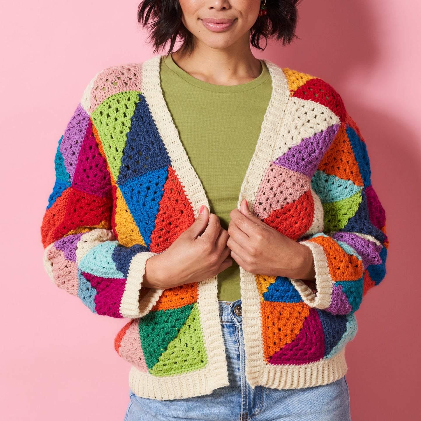 Person wearing a colorful crocheted cardigan against a pink background