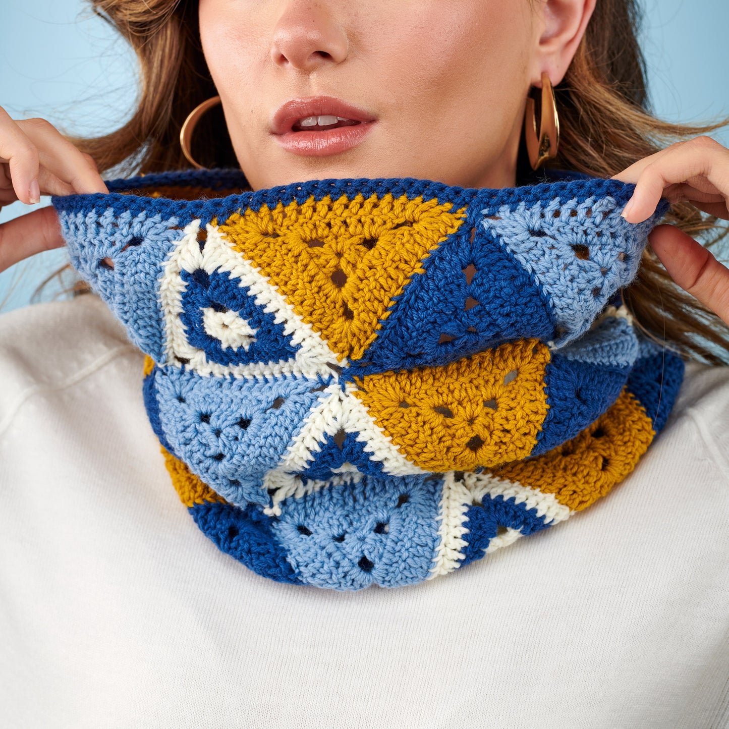 Person wearing a colorful crocheted cowl with geometric patterns.