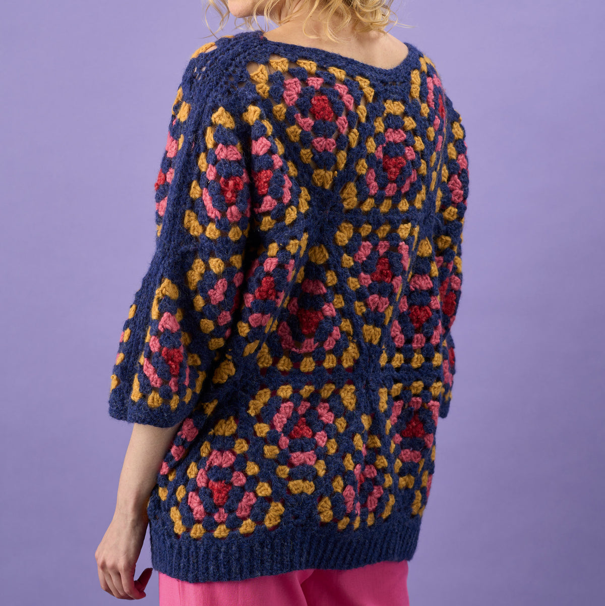 Person wearing a colorful crochet sweater against a purple background